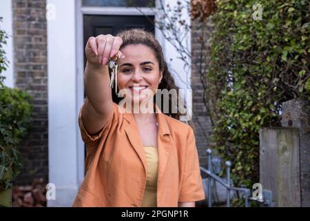 Donna sorridente che tiene nuove chiavi fuori casa Foto Stock