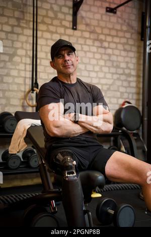 Uomo maturo che indossa una gamba protesica con le braccia incrociate in palestra Foto Stock