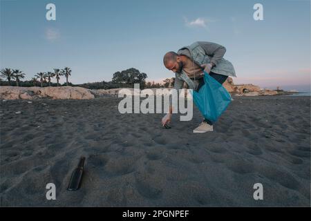 Uomo che raccoglie i rifiuti in sacchetto di plastica dalla spiaggia Foto Stock