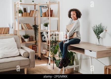 Ragazza sorridente seduta sulla scrivania di casa Foto Stock