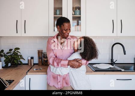 Nonna abbracciando la nonna in cucina a casa Foto Stock