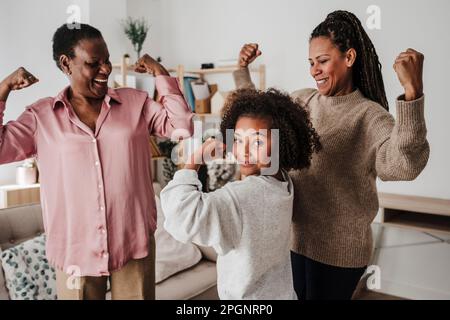 Ragazza che flette i muscoli con madre e nonna a casa Foto Stock