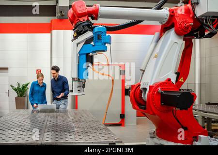 Colleghi aziendali che lavorano su un computer portatile in una fabbrica di robot Foto Stock