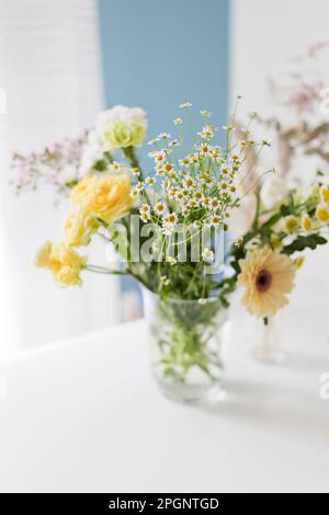 Fiori gialli e bianchi in vaso di vetro su tavola Foto Stock