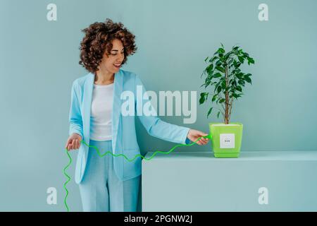Donna sorridente che inserisce la presa collegata alla pianta in vaso Foto Stock
