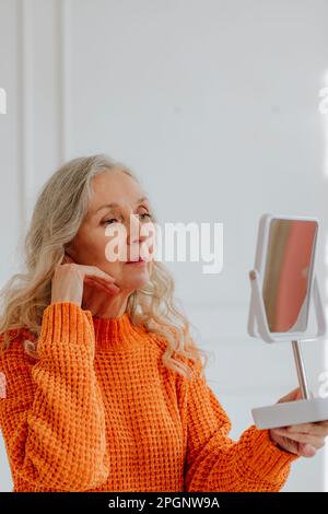 Donna anziana che guarda nello specchio a casa Foto Stock