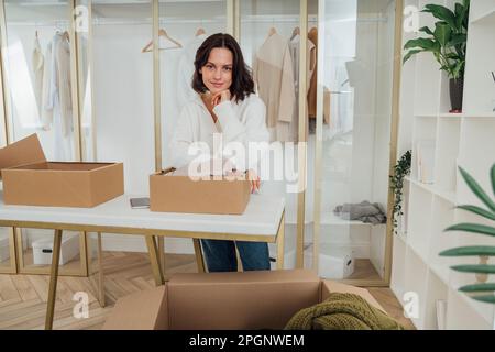 Donna sorridente con la mano sul mento appoggiata sulla scatola a casa Foto Stock