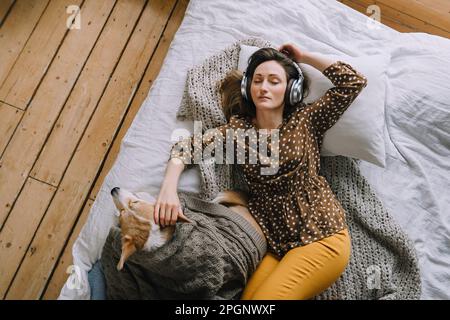 Donna spensierata che ascolta la musica attraverso le cuffie sdraiate sul letto a casa Foto Stock