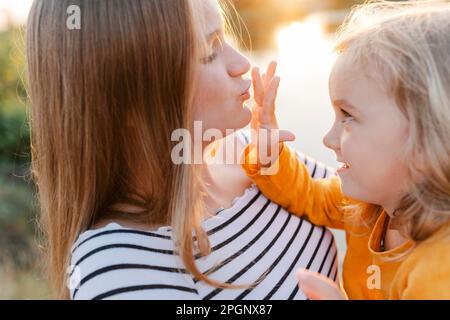 Sorridente ragazza carina che tocca le sorelle faccia e abbraccia al tramonto Foto Stock