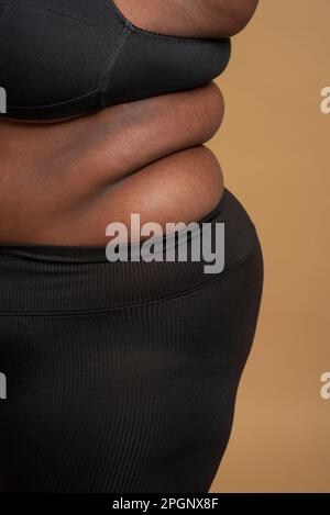Primo piano di pancia e rotoli posteriori di più dimensione donna su sfondo beige Foto Stock