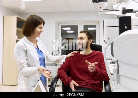 Oftalmologo sorridente che parla con il paziente seduto in clinica Foto Stock
