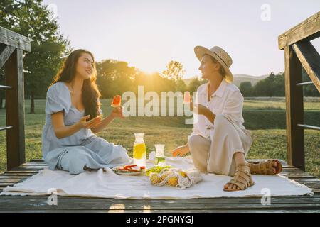 Donne felici che tengono fette di anguria seduto su coperta da picnic Foto Stock