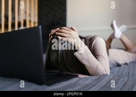 Donna stanca sdraiata sul letto con un computer portatile a casa Foto Stock