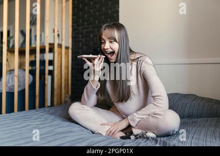 Donna felice che parla sul telefono altoparlante alla camera da letto Foto Stock