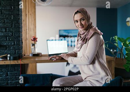 Freelance che indossa hijab seduto al tavolo in ufficio a casa Foto Stock