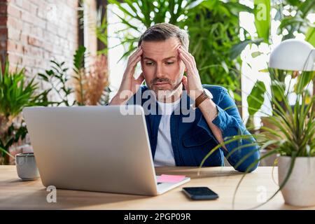 Uomo d'affari preoccupato con un computer portatile alla scrivania in un ufficio loft Foto Stock