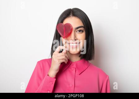 Donna felice con lollipop a forma di cuore su sfondo bianco Foto Stock