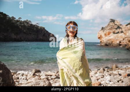 Donna avvolta in coperta dopo aver nuotato in spiaggia Foto Stock