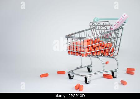 carrello del supermercato pieno di pillole arancioni e un metro su uno sfondo bianco. spazio di copia. concetto di dipendenza a pillole di perdita del peso Foto Stock