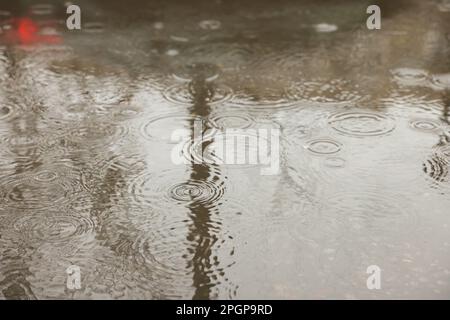 Gocce di pioggia che cadono sulla pozza all'aperto Foto Stock