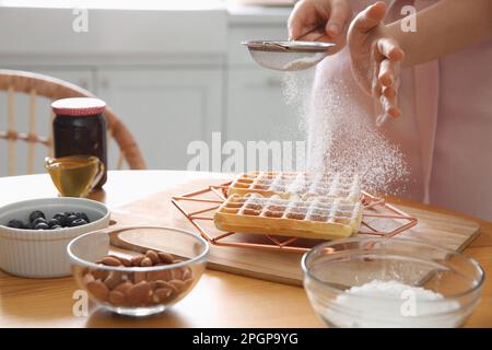 Donna decorazione deliziosi waffle belgi con zucchero a velo al tavolo in legno in cucina, primo piano Foto Stock