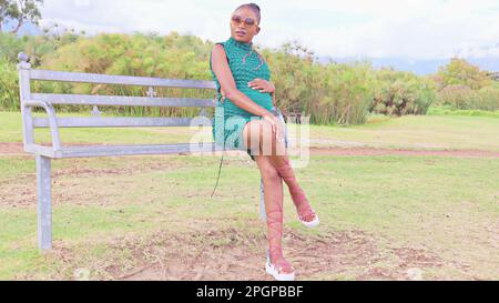 donna incinta nera seduta su una panchina nel parco Foto Stock