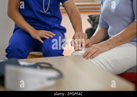 Immagine ritagliata di un medico gentile che tiene o tocca la mano di un paziente per comodità e sostegno. Una vecchia paziente ammalata viene rassicurata dal medico. Foto Stock