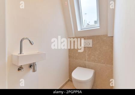 un bagno bianco in un piccolo bagno con piastrelle beige alle pareti e un lucernario sopra la finestra Foto Stock