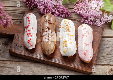 Dessert vari eclair. Su tavola in legno con fiori di lilla Foto Stock