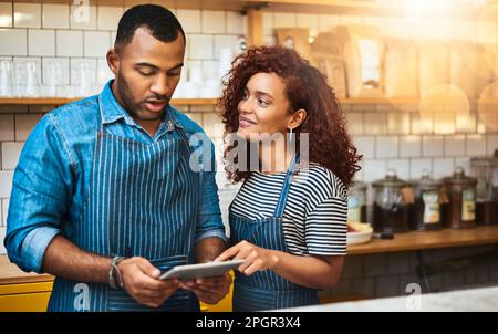 Questo sembra buono. una giovane coppia affettuosa che lavora su una tavoletta nel suo bar. Foto Stock