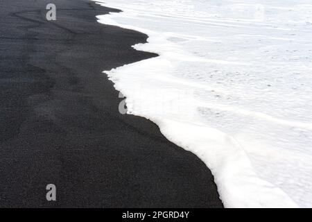 Bianco onda schiumosa lavaggio su una spiaggia di sabbia nera. Concetto creativo di pace, armonia ed equilibrio di fondo. Foto Stock