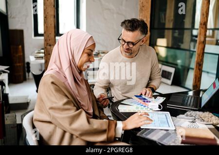 Due allegri colleghi multinazionali designer che lavorano insieme ai computer in un accogliente workshop Foto Stock