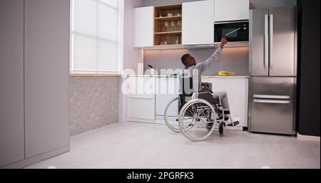 Uomo Disabile Usando Lo Strumento Grabber Per Controllare Il Forno A Microonde In Cucina Foto Stock