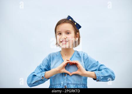 Sorridente bambina fare segno di cuore con le mani in abito denim casual isolato su sfondo bianco, studio, fa l'icona dell'amore, gesto con le dita cuore Foto Stock