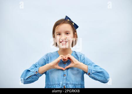 Sorridente bambina fare segno di cuore con le mani in abito denim casual isolato su sfondo bianco, studio, fa l'icona dell'amore, gesto con le dita cuore Foto Stock