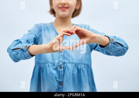 Sorridente bambina fare segno di cuore con le mani in abito denim casual isolato su sfondo bianco, studio, fa l'icona dell'amore, gesto con le dita cuore Foto Stock