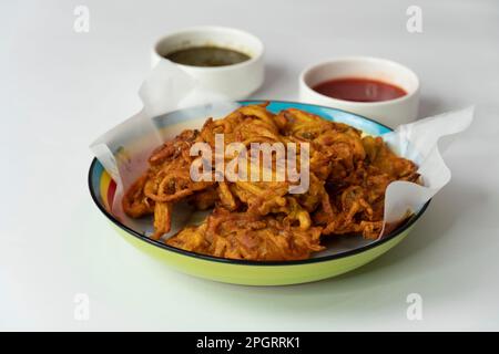 Pakora di cipolla fritta preferito indiano-pakistano tè-tempo spuntino durante la stagione piovosa. servito con salsa alla menta e peperoncino dolce su fondo testurizzato Foto Stock