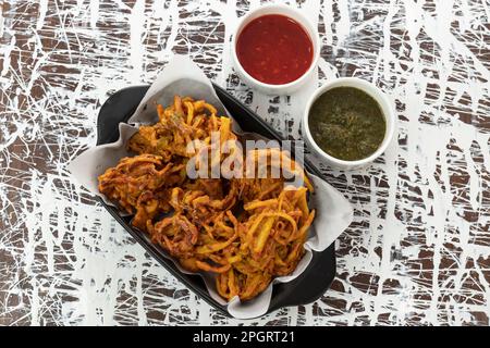 Pakora di cipolla fritta preferito indiano-pakistano tè-tempo spuntino durante la stagione piovosa. servito con salsa alla menta e peperoncino dolce su fondo testurizzato Foto Stock