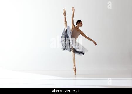 Ballerina giovane e incredibilmente bella sta posando e ballando in uno studio bianco. Balletto classico Foto Stock