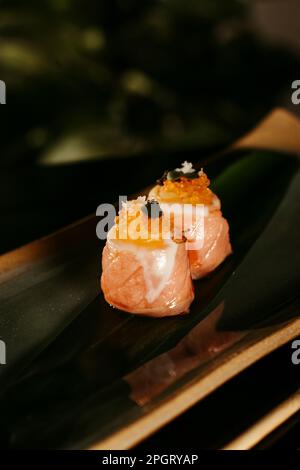 Questa immagine presenta una delicatezza di sushi presentata in modo artistico su un piatto nero con un bordo dorato Foto Stock