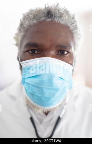 afroamericano medico senior maschile guardando la fotocamera indossare maschera facciale. medico al lavoro durante la pandemia di coronavirus covid 19. Foto Stock