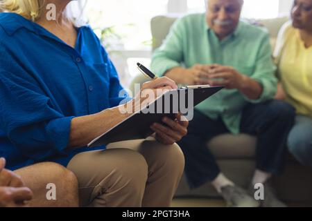 Gruppo di diversi amici anziani seduti in soggiorno, parlando in gruppo di terapia sessione. Stile di vita, amicizia e supporto senior. Foto Stock