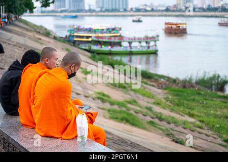 Phnom Penh, Cambogia-Dicembre 23rd 2022: Vestito con i loro tradizionali vesti arancioni vibranti, due monaci Khmer, vicino al Palazzo reale, sedersi di fronte alla Tonle SA Foto Stock