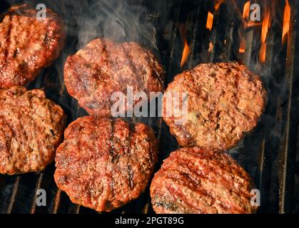 Primo piano di ricerca e fumo manzo o carne di maiale barbecue hamburger per hamburger su barbecue fuoco griglia con griglia in ghisa metallo, vista ad alto angolo Foto Stock