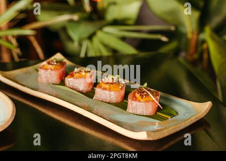 Un piatto bianco riempito con una varietà di sushi roll e servito su uno sfondo sfocato Foto Stock