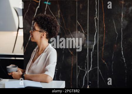 Donna d'affari di mezza età che beve caffè mentre si siede al tavolo in ufficio Foto Stock