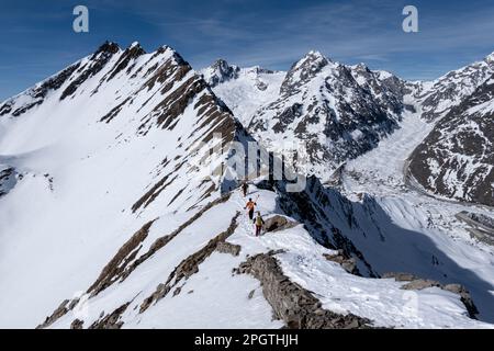 Courmayeur, Italia - 18 Febbraio, 2023: 3 sciatori che camminano lungo una stretta e ripida cresta di montagna innevata nel massiccio del Monte Bianco Foto Stock