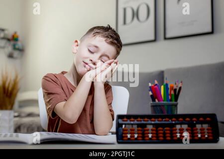 Il ragazzo seduto al tavolo, studiava matematica, si stanca, si posò sulle mani e chiuse gli occhi. Foto Stock