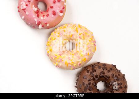 Tre ciambelle in fila - bianco, rosa e cioccolato su uno sfondo bianco vista dall'alto Foto Stock