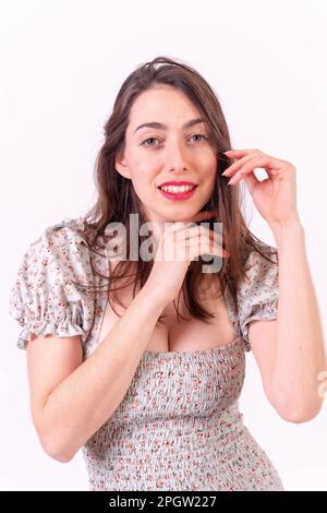 Un'attraente femmina caucasica che indossa un abito a motivi floreali bianco su sfondo bianco Foto Stock